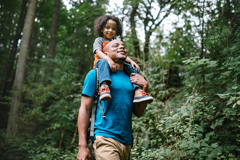 Man with child on shoulders walking through a forest