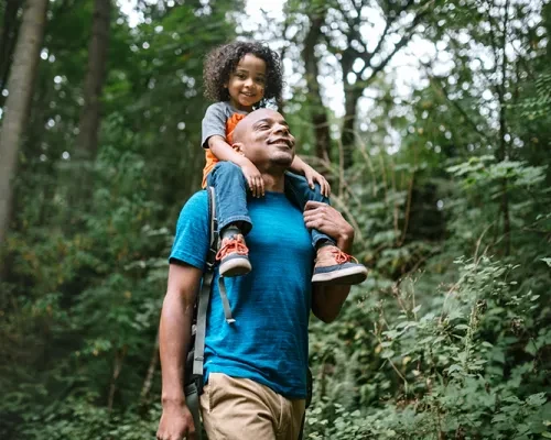 Man with child on shoulders walking through a forest
