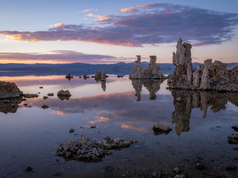 Tufa towers at Mono Lake Tufa State Natural Reserve reflected in calm evening water under pink and lavender clouds.