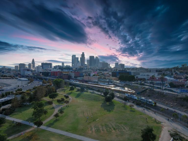 View of Los Angeles State Historic Park with open green space, walking paths, and the downtown Los Angeles skyline in the background.