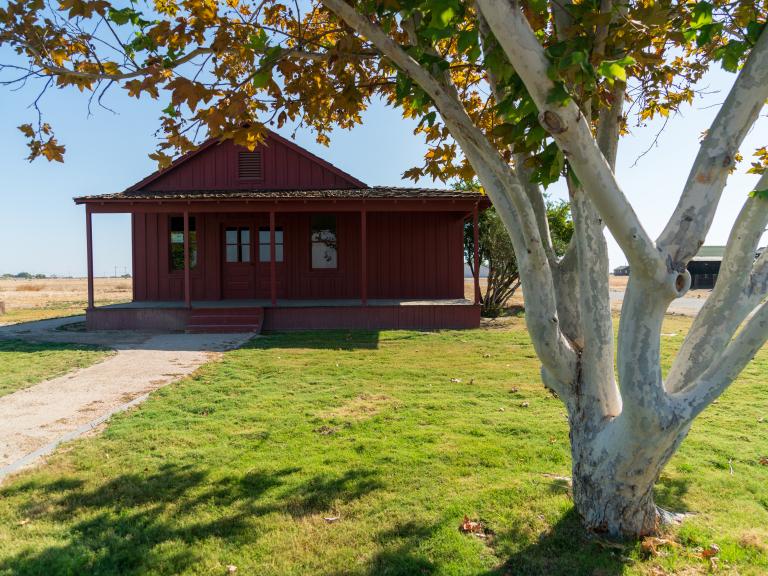 The General Store at Colonel Allensworth State Historic Park shown as a red wooden house with a lawn, pathway, and tree in front