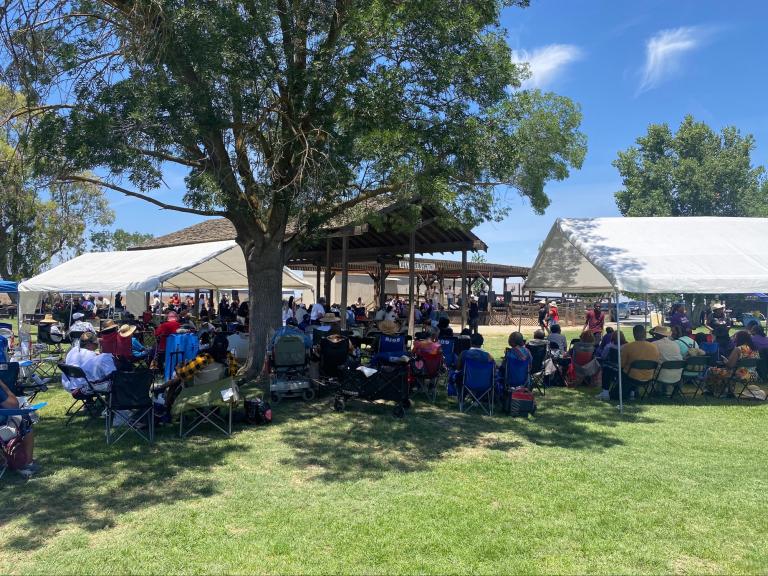 Juneteenth Celebration at Colonel Allensworth SHP. A crowd sits in folding chairs under trees and tents at an outdoor event on a sunny day.