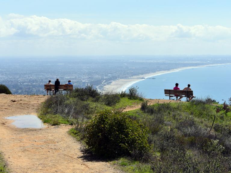 Visitors seated at a scenic overlook in Topanga State Park, with sweeping views of the Pacific Ocean, Santa Monica Bay, and the Los Angeles coastline.