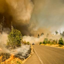 brush fire and plumes of smoke next to a long highway