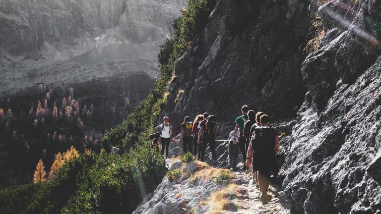 group hiking along rock wall ledge heading towards a mountainous forest