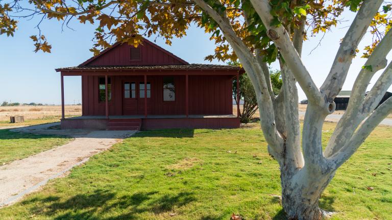 The General Store at Colonel Allensworth State Historic Park shown as a red wooden house with a lawn, pathway, and tree in front