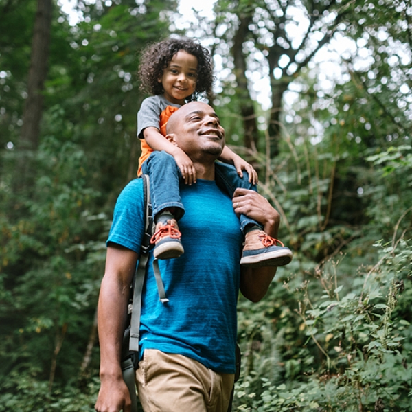 Man with child on shoulders walking through a forest