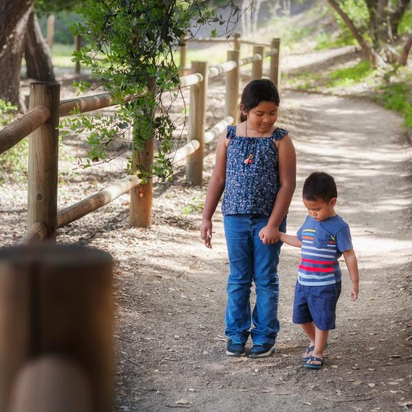 Family holding hand while walking in a wooded pathway in a California park.