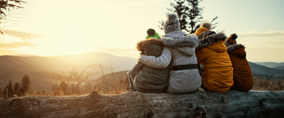 People sitting on fallen tree branch watching sunset in winter. 