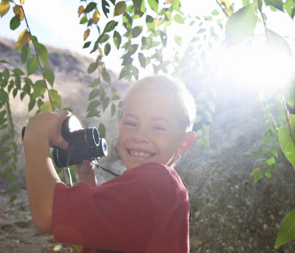 Side view portrait of a smiling young boy with binoculars